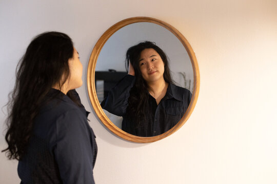 Asian American trans woman looking in the mirror.
