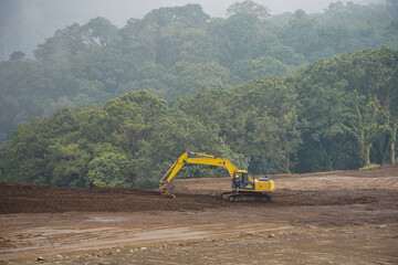 Heavy machine clearing land near green forest