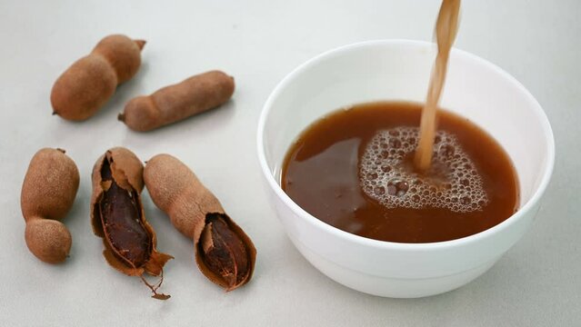 Serving tamarind water in a bowl and raw tamarind in the background.
