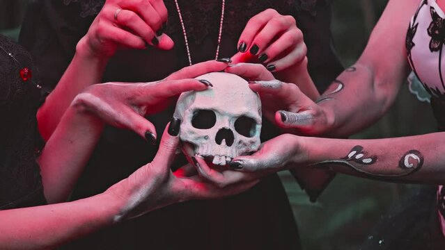 Three Young Women with a design on the face and neck in the style of the Goddess of Death or Katarina conjure over a sugar skull while holding it in their hands. Close-up on hands