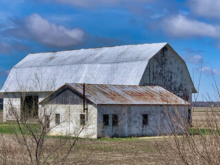 View of farm buildings on a corn field behind dry branches.