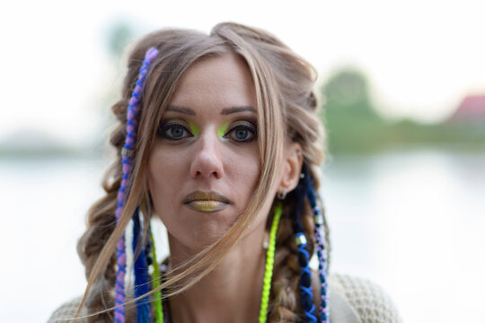 portrait of a girl looking at the camera, with bright multi-colored braids, close-up on the background of the lake