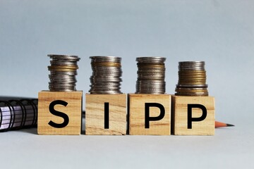 SIPP (Self Invested Personal Pension) - acronym on wooden cubes on coins on a white background....