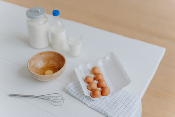 Baking ingredients on white table. Eggs, milk and flour in containers. Beater for whisking and making dough. Process of baking. Time to cook