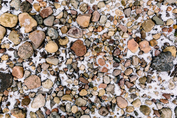 First snow or hail covered stones. Textured background. The track pattern made of natural material. Red and gray colors pebbles on a beach in winter season. Covering the pedestrian area. Garden path