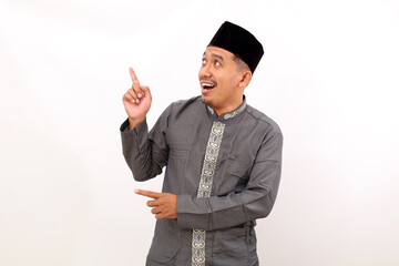 Happy asian muslim man standing while pointing something above and beside him. Isolated on white background