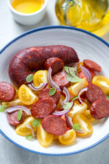 Closeup of salad with yellow tomatoes, warm chorizo sausage and red onion, vertical shot, selective focus