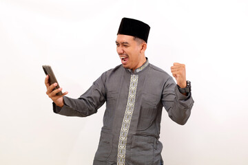 Surprised asian muslim man standing while getting a good news from his phone. Isolated on white background