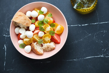 Roseate bowl with mini mozzarella and tomato salad, above view on a black marble background, horizontal shot with copy space