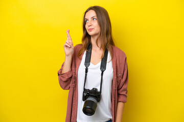 Young photographer caucasian woman isolated on yellow background with fingers crossing and wishing the best