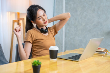 Female college student in headphones typing homework report on laptop until feeling pain in shoulders and stretching arms. office syndrome concept