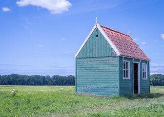 Dutch landscape with green grass, an old abandoned wooden building and a blue sky