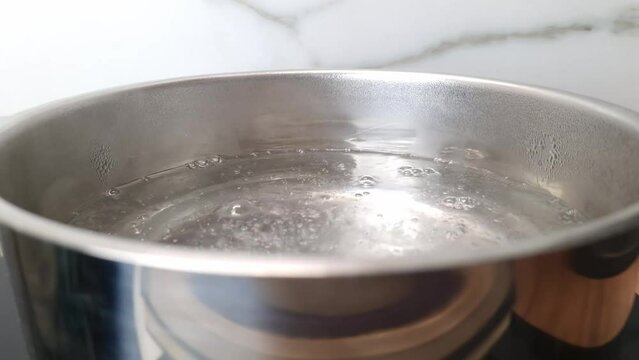 Water starts to boil in pot on stove at the kitchen. Boiling process