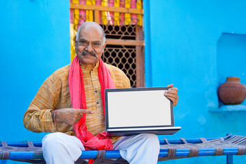 Indian farmer showing laptop screen at home. - obrazy, fototapety, plakaty