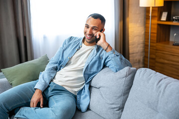 Happy man in casual clothes sitting on couch and answering phone call at home