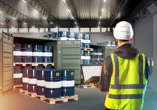 Auditor in warehouse with oil barrels. Man with laptop with back to camera. Auditor guy is inspecting fuel storage. Barrels with oil in shipping containers. Warehouse auditor inside hangar