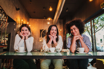 Portrait of thee young women smiling and posing looking at camera on a coffee shop. Photo of a group of happy females on a restaurant or bar. High quality photo