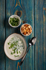 yogurt soup with herbs and crackers on a blue wooden table,top view