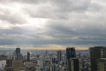 Overhead view of Osaka's Umeda area from a hill on a cloudy day, sunlight shining through a gap in the clouds.
