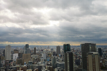 Overhead view of Osaka's Umeda area from a hill on a cloudy day, sunlight shining through a gap in the clouds.