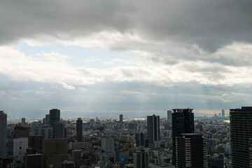 Overhead view of Osaka's Umeda area from a hill on a cloudy day, sunlight shining through a gap in the clouds.