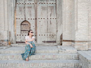 Beautiful young woman against the backdrop of landmarks and ancient buildings. Sights of ancient cities of Uzbekistan. Clear, sunny day. Vacation and travel concept
