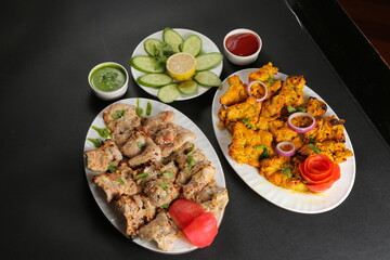 Chicken tikka black background served with green salad and sauces 