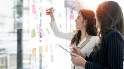 Young  businesswoman creative team using post it notes in glass wall to writing strategy business...