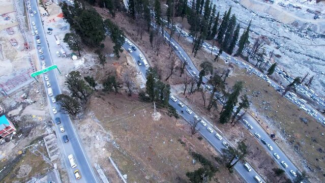 aerial drone shot showing cars stuck in line in massive traffic jam to base of valley on winding serpentine road leading to atal tunnel from Manali surrounded by snow and trees a popular tourist spot