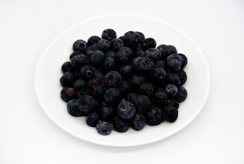 Delicious and juicy blueberries on a white plate on a white background. Large blueberry yayagods.