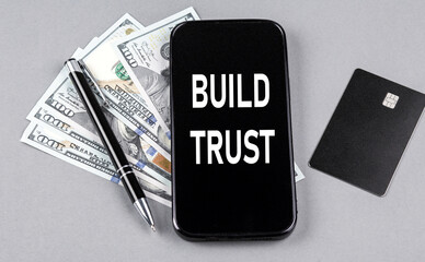 Credit card and text BUILD TRUST on smartphone with dollars and pen. Business concept