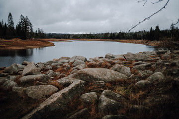 View of the Oder pond in the Harz Mountains in autumn. The Oder was dammed here by the historic dam and lies idyllically in the forest. In the foreground are stones.