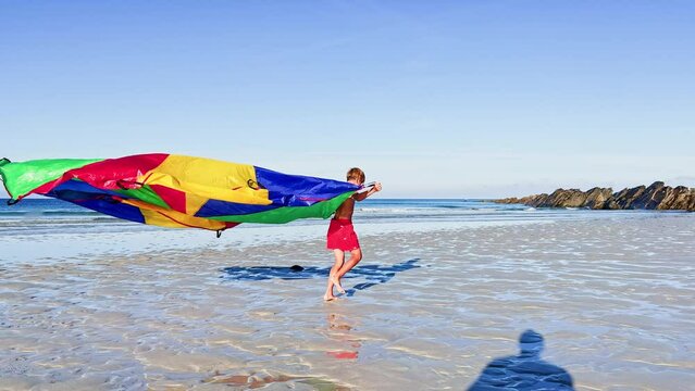 Child with colorful parachute fabric run on beach