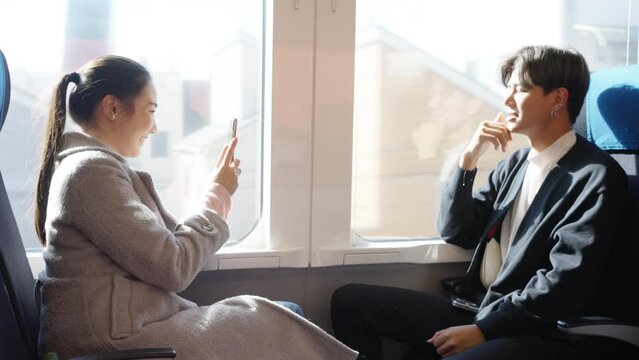 Happy Asian couple tourist sitting by the window and using mobile phone photography together while travel Japan on train. Railway transportation and winter autumn holiday vacation in Japan concept.