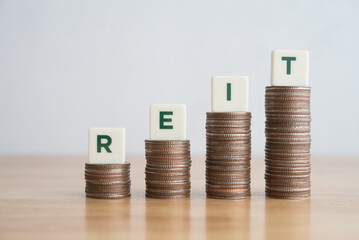 Word REIT on stack coins as growth capital gains graph chart on wooden table background white wall background copy space. Real Estate Investment Trust (REIT) investment and money risk management.