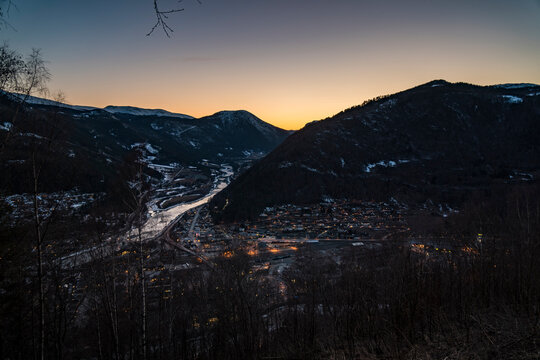 Twilight winter landscape of Otta, Norway with glowing lights in valley and surrounding mountains