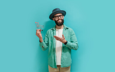 A young hipster man dressed casual holding a mini shopping cart isolated on blue studio background....