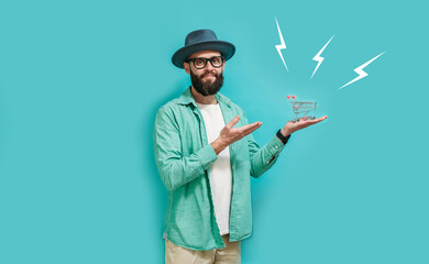 A young hipster man dressed casual holding a mini shopping cart isolated on blue studio background....