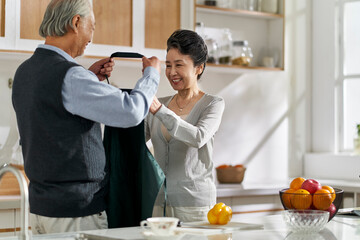 senior asian man helping wife putting on apron