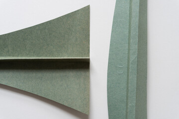 two folded and cut green paper card objects on blank paper