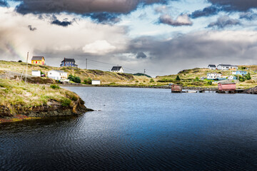 Small rustic colourful beach homes and cottage living on rocky headlands with a boat house under a dramatic sky near Port Rexton Newfoundland Canada.