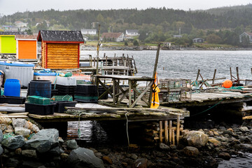 Colourful fishing tackle sheds and boat docks along a rocky beach on the East Coast of Canada at Heart's Content Newfoundland under a stormy sky.