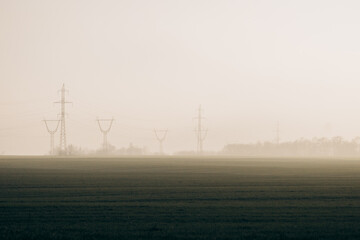 Power lines in the middle of a field with fog during the day. energy crisis