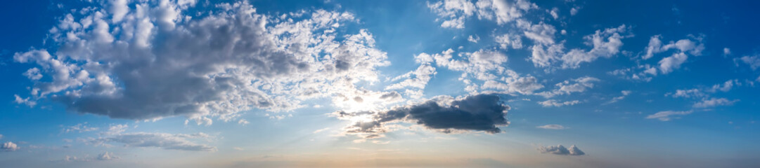 Panoramic view of sunset sky with clouds and sun.