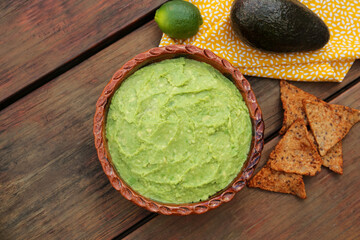 Delicious guacamole, avocados and nachos on wooden table, flat lay