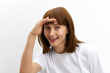 a funny, funny, cheerful woman stands on a white background in a white T-shirt and leaning her hand to her forehead looks at the camera smiling sweetly