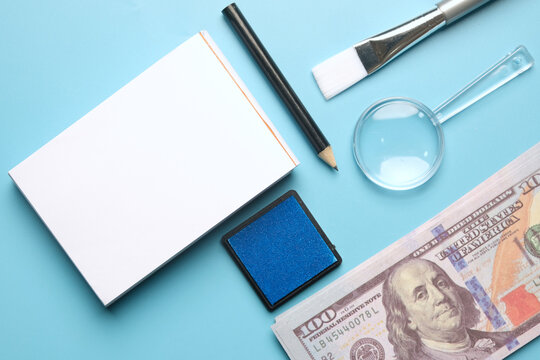 A flatlay picture of fingerprint pad on fake cash, copyspace notepad, pencil magnifying glass, safety glass, puffer, brush and inkpad. Forensic accounting concept.