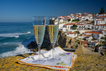 Glasses of champagne sparkling wine and view on white houses of picturesque village Azenhas do mar,...