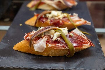 Typical snack of Basque Country, pinchos or pinxtos, small piece of bread with fish, jamon and different toppings, served in bar in San-Sebastian or Bilbao, Spain