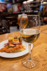Board with typical snacks of Basque Country, pinchos or pinxtos, skewers or small piece of bread with toppings, served with glass of txakoli wine in bar in San-Sebastian or Bilbao, Spain